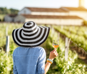 Woman with a hat drinking a glass of wine and appreciating a vineyard

